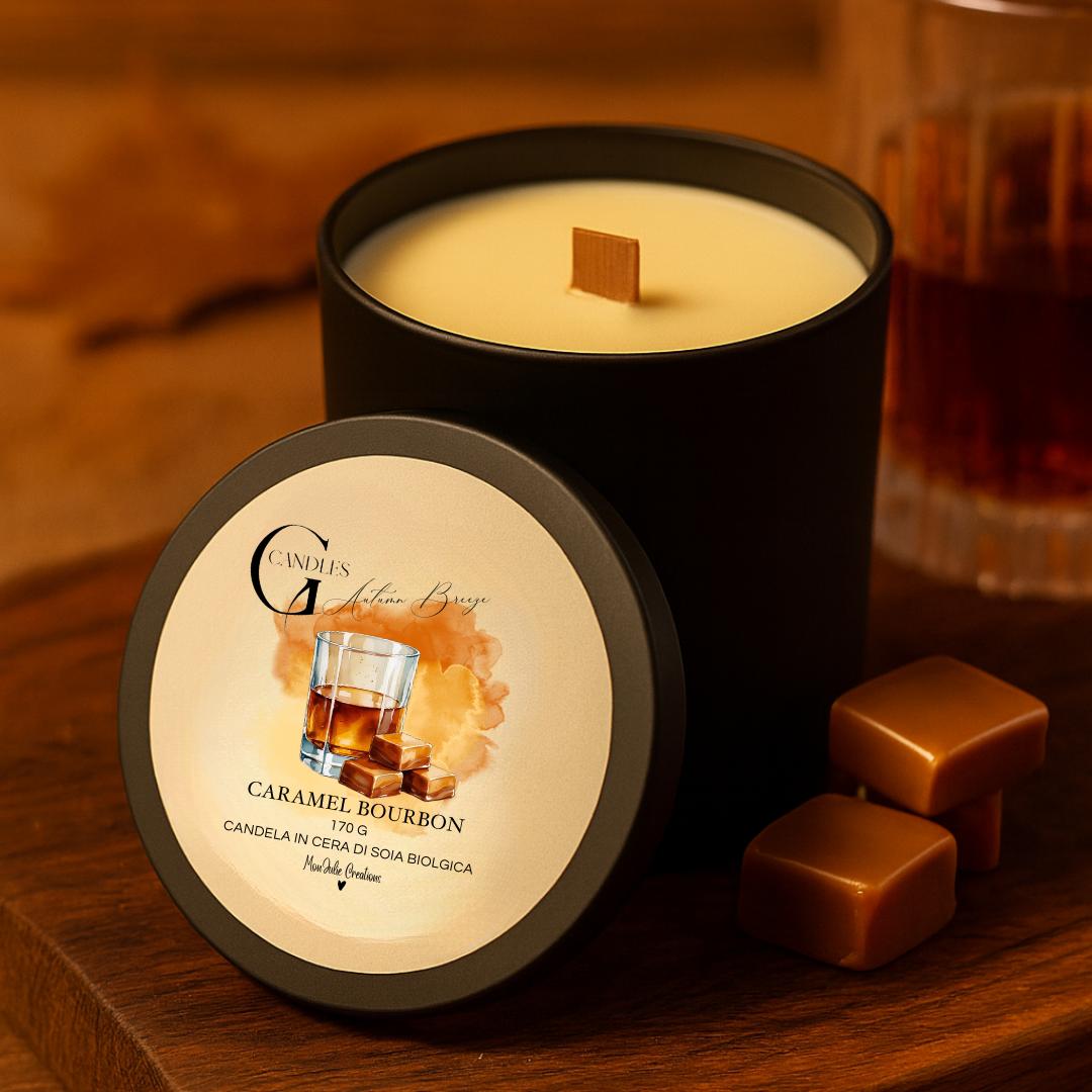 Candela profumata al gusto di bourbon e caramello in cera di soia biologica colata a mano in barattolo di alluminio nero con stoppino in legno, decorata con illustrazioni di bicchiere con liquido ambrato e cubetti di caramello, su sfondo con colori caldi, autunnali, elementi in legno.