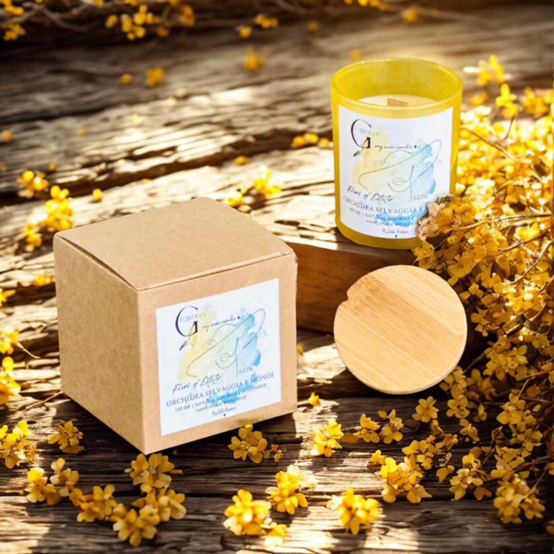 Candela in cera di soia in vasetto di vetro giallo con grafica realizzata a mano e scatolina kraft, decorata con fiori gialli secchi.