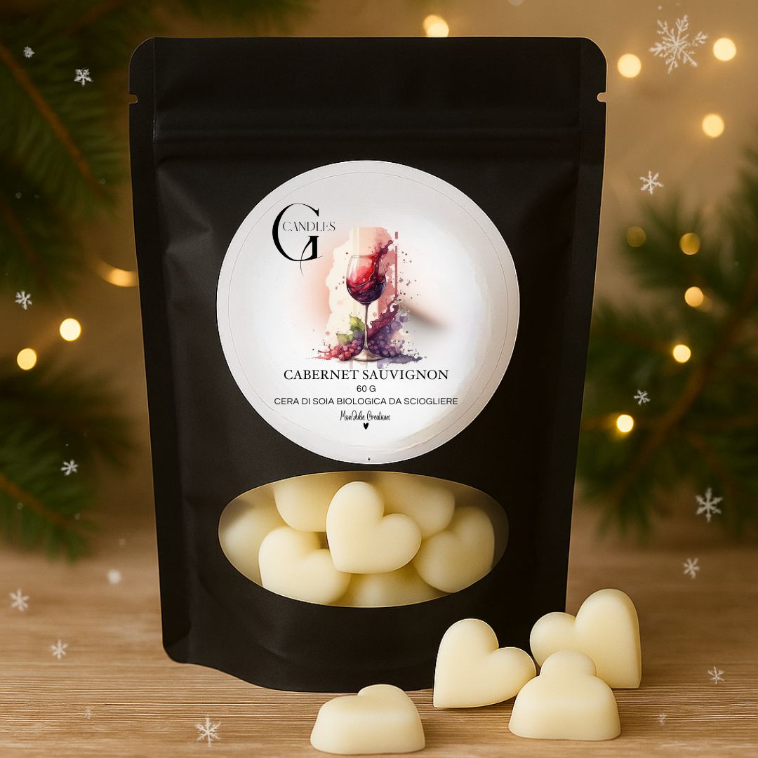 Wax melts al profumo di vino rosso Cabernet Sauvignon, in cera di soia biologica, in bustina nera con finestra trasparente, grafica raffinata. Sfondo con piano in legno naturale e cuoricini in cera decorativi.