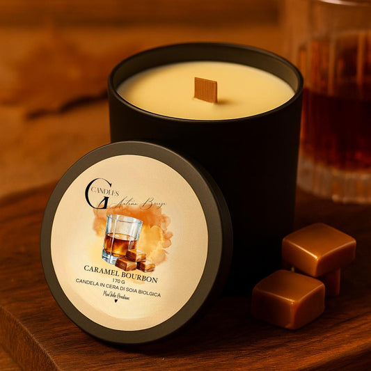 Candela profumata al gusto di bourbon e caramello in cera di soia biologica colata a mano in barattolo di alluminio nero con stoppino in legno, decorata con illustrazioni di bicchiere con liquido ambrato e cubetti di caramello, su sfondo con colori caldi, autunnali, elementi in legno.