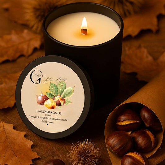 Candela al profumo di caldarroste, in cera di soia artigianale, in batrattolino di allumino nero, ambientata con castagne  in cartoccio di cara kraft, ricci e foglie autunnali.