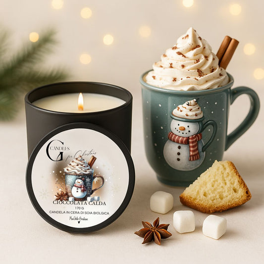 Candela natalizia al profumo di cioccolata calda in cera di soia biologica, artigianle, in barattolino nero di alluminio con coprechio, grafica natlalizia raffinata. Sfondo in legno chiaro con rami di abete e piccoli marshmallows, tazza mug blu con pupazzo di neve, panna montata, stecca di cannella ed elementi decorativi.