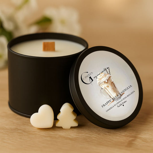 Candela al profumo di frappè alla vaniglia, in cera di soia biologica, artigianale, in barattolino nero di alluminio con coperchio e grafica raffinata. Sfondo in legno chiaro con piccole wax melts decorative a forma di cuore e alberello.