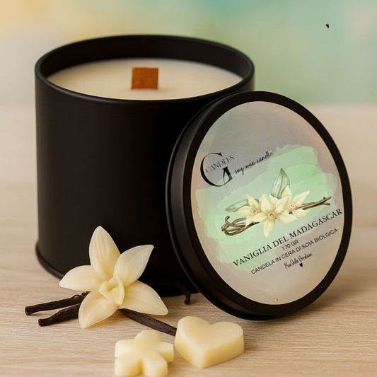 Candela al profumo di vaniglia del Madagascar, in cera di soia biologica, artigianale in barattolino nero in alluminio con coperchio e grafica raffinata. Sfonfo in legno chiaro, con decorazioni di piccole wax melts, cuorico, fiori e bacello di vaniglia.