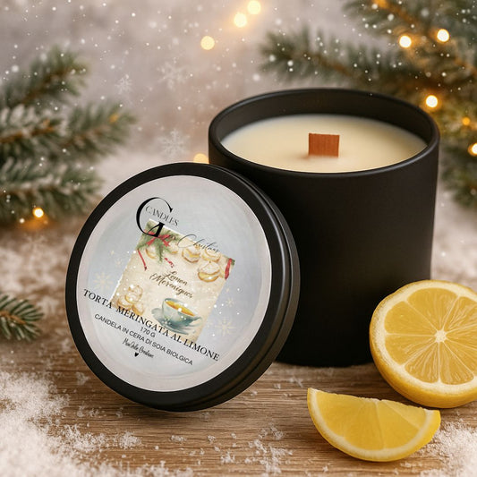 Candela natalizia al profumo di torta meringata al limone, in cera di soia biologica, artigianale in barattolino nero di alluminio con coperchio e grafica raffinata. Sfondo in legno chiaro innevato, limone, rami di pino e lucine decorativi.