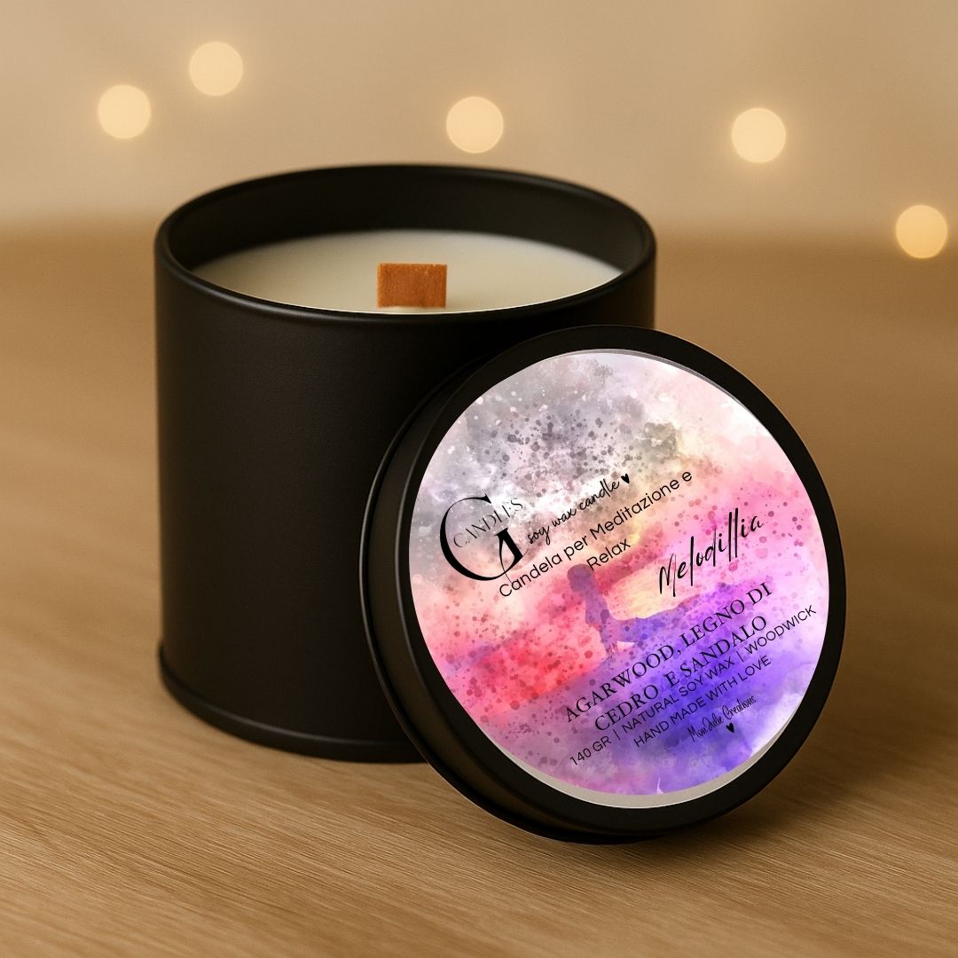 Candela per meditazione al profumo di agarwood e legno di cedro in cera di soia, artigianale in barattolino nero in alluminio, con grafica raffinata, sfondo chiaro con lucine e piano in legno chiaro.