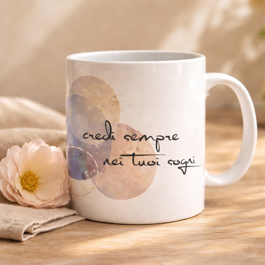 Tazza mug in ceramica bianca, con frase motivazionale e cerchi nei colori pastello, grafica e stampa artigianali, con fiore bianco e tovagliolo come elementi decorativi.