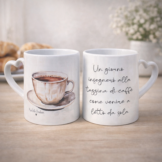 Tazza mug in ceramica bianca con manico fronte e retro a cuore, grafica con tazzina da caffè e frase ironica e divertente, realizzata a mano, su piano in legno chiaro, fiori e croissant sullo sfondo.